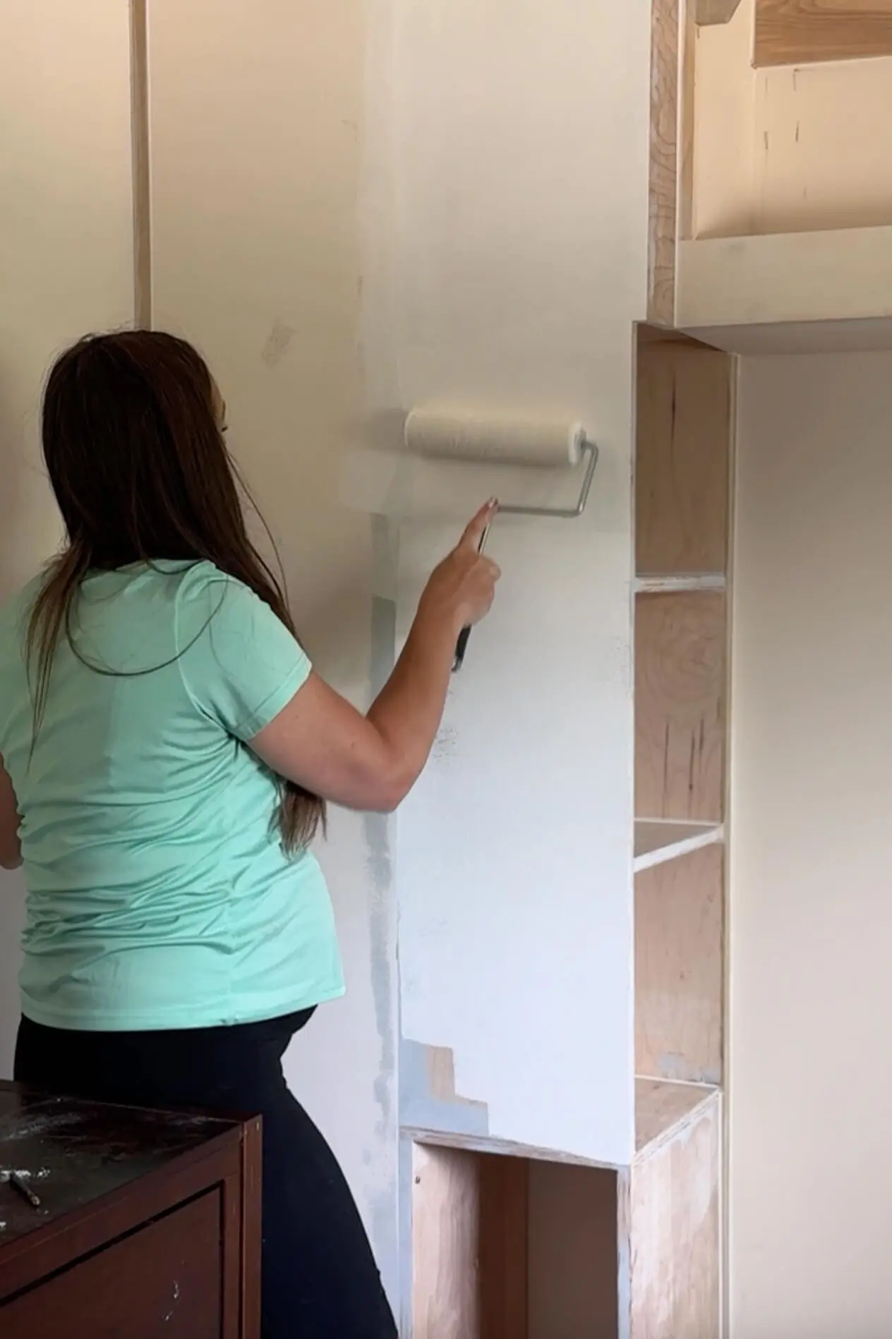 Applying primer over wood filler and Bondo to prep a custom-built nursery wall unit for paint.